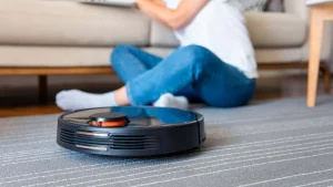 Robot aspirador limpiando alfombra cerca de una persona sentada en el suelo