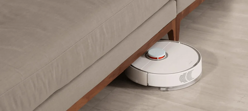 Robot aspirador accediendo debajo de un sofá de tela en una casa moderna